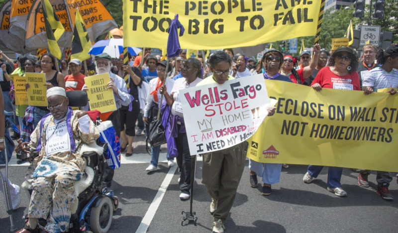 A photo of a protest march against Wells Fargo, people are holding banners decrying bankers